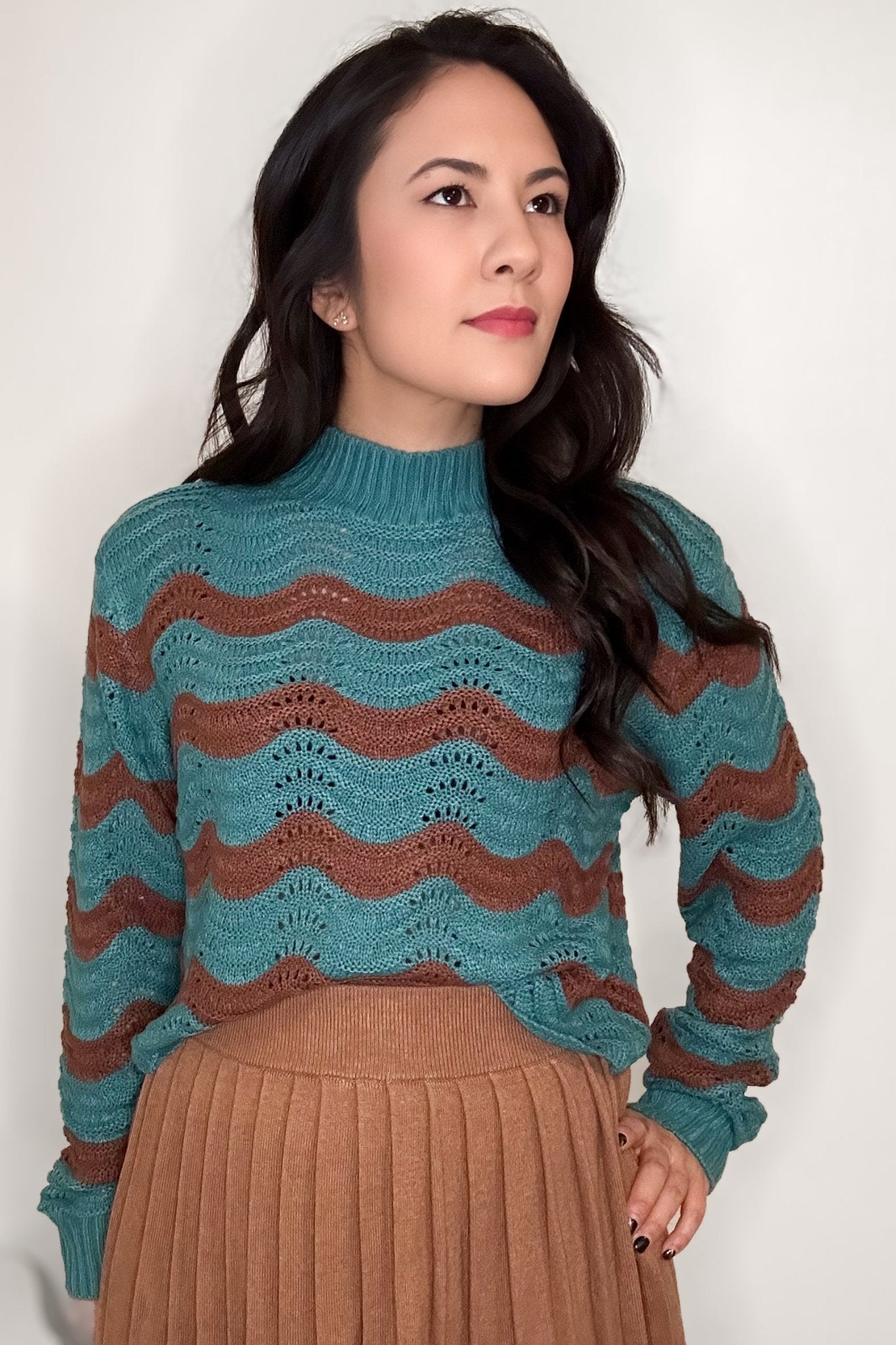 A woman wearing a turquoise and brick striped colored mock neck sweater with a camel colored skirt