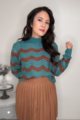 A woman wearing a turquoise and brick striped colored mock neck sweater with a camel-colored skirt