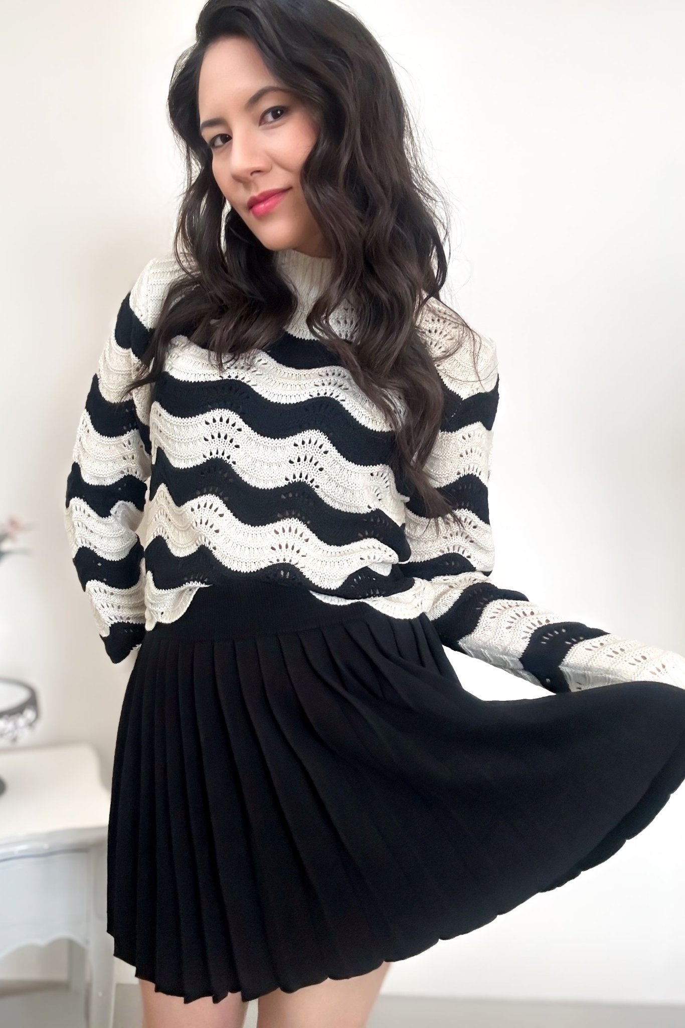 Woman wearing a striped sweater with a black-colored pleated mini skirt