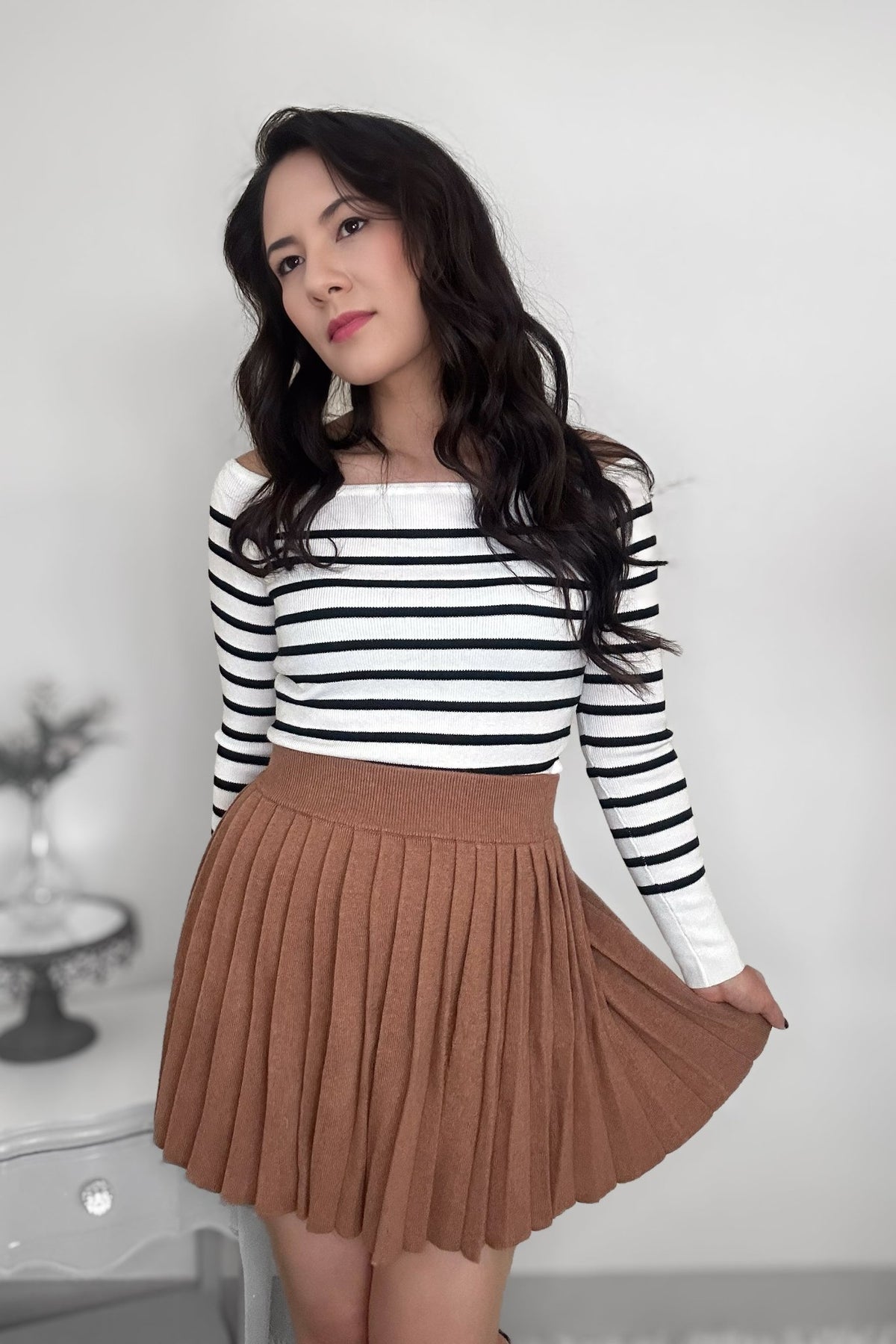 Woman wearing a striped sweater with a camel-colored pleated mini skirt