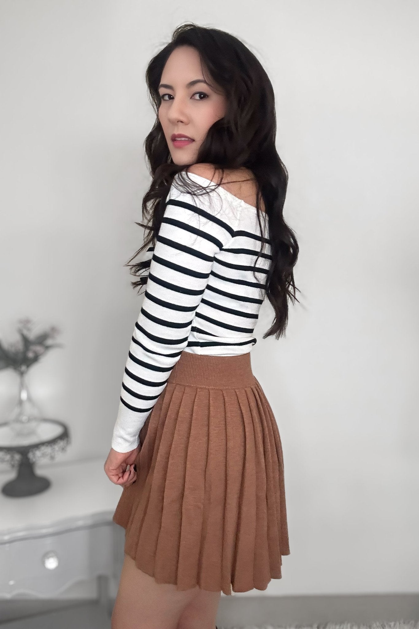 Woman wearing a striped sweater with a camel-colored pleated mini skirt