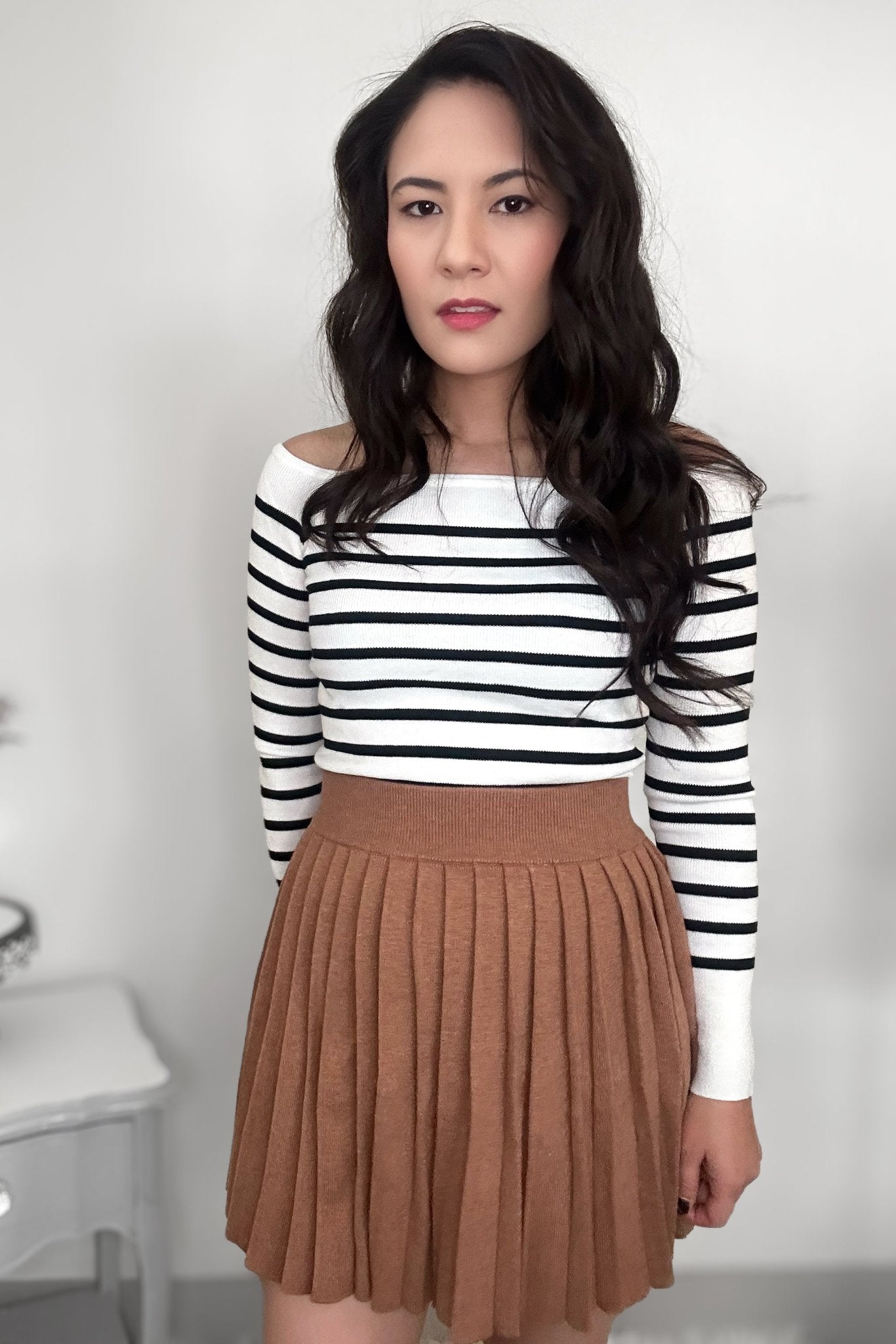 Woman wearing a striped sweater with a camel-colored pleated mini skirt