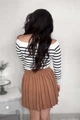 Back view of woman wearing a striped sweater with a camel-colored pleated mini skirt