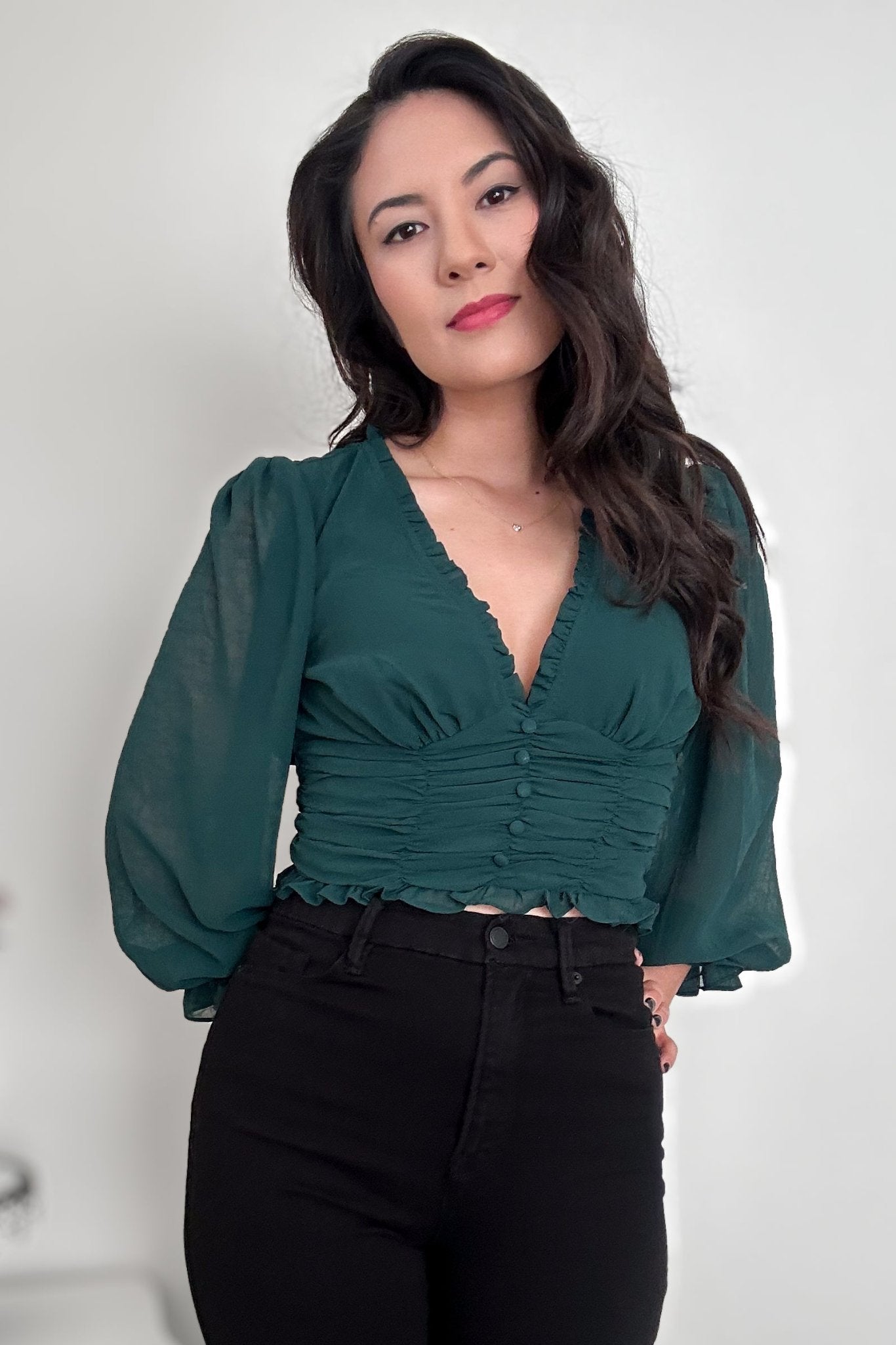 Woman wearing a green V-neck blouse with balloon sleeves with black pants 