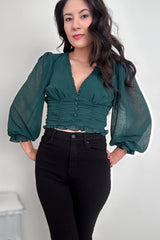 Woman wearing a green V-neck blouse with balloon sleeves with black pants