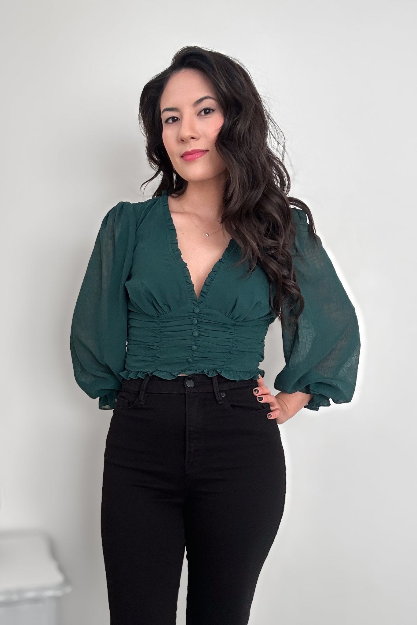 Woman wearing a green V-neck blouse with balloon sleeves with black pants 