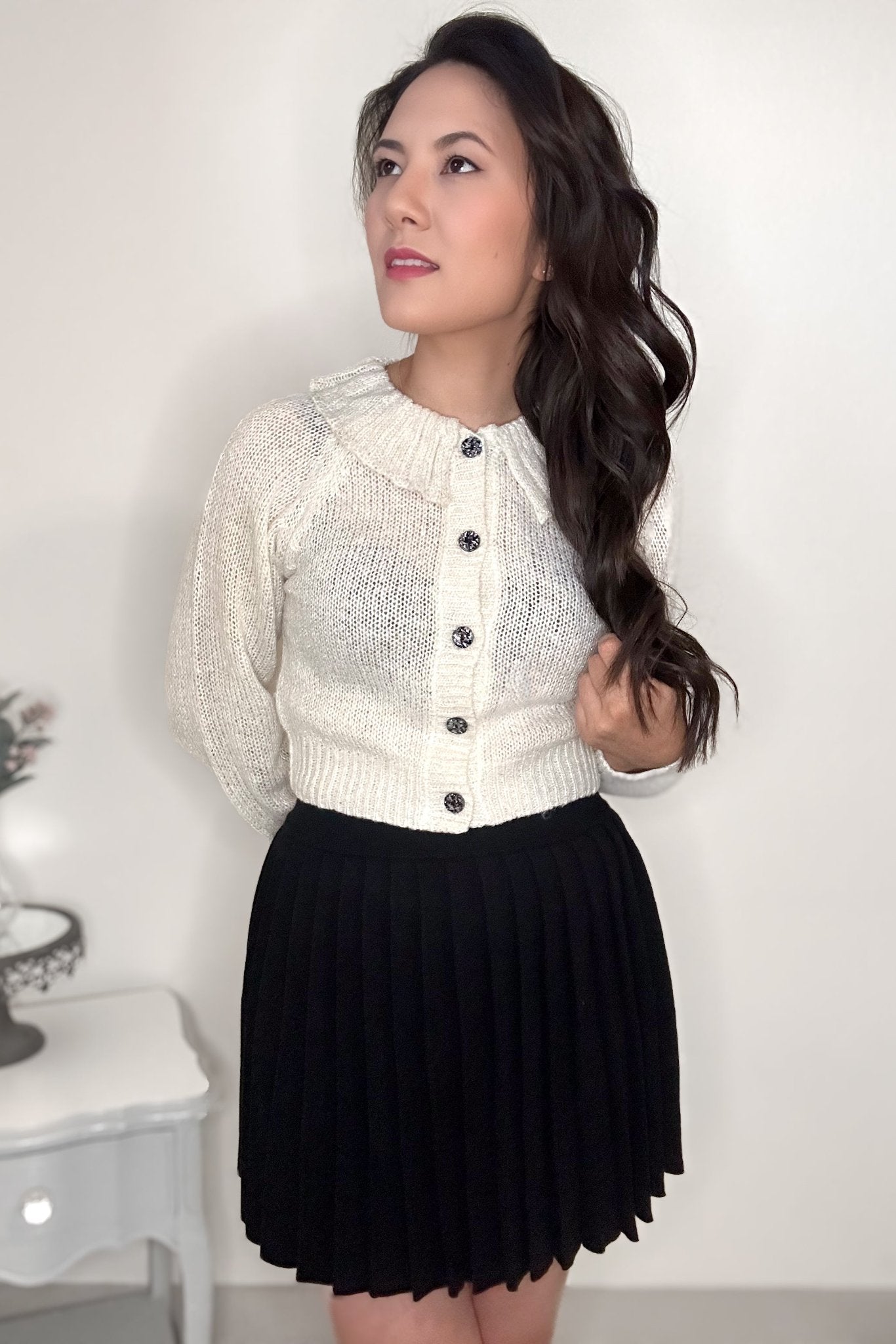 Woman wearing an off-white cardigan and black pleated mini skirt