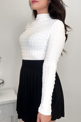 Side view of a woman wearing an off-white textured mock neck shirt and a black pleated mini skirt